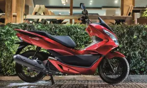 Czerwony skuter Honda PCX, jeden z popularnych **marek skuterów**, zaparkowany przed zielonym żywopłotem.