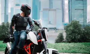 Motocyklista w zbroi ochronnej siedzi na motocyklu na tle wieżowców.