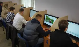 Ludzie siedzą przy komputerach, rozwiązując testy. Zastanawiasz się, ile czasu trwa egzamin teoretyczny na prawo jazdy?