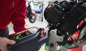 Osoba w czerwonej bluzie wlewa olej Motul do silnika motocykla crossowego 4T.