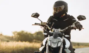 Motocyklista w kasku i kurtce siedzi na motocyklu na tle krajobrazu.