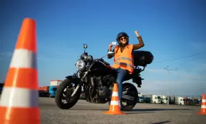 Szczęśliwa motocyklistka z prawem jazdy kategorii A2 na motor 250, świętuje sukces na placu manewrowym.
