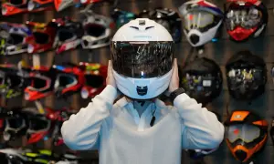 Osoba przymierza biały kask motocyklowy Schuberth. W tle widać rząd kolorowych kasków, co sugeruje budowę kasku motocyklowego.