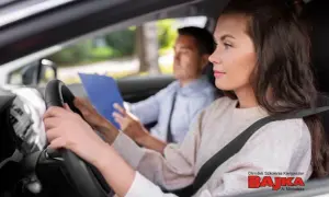 Młoda kobieta uczy się jeździć, a instruktor z notatkami obok. Dowiedz się, ile się robi prawo jazdy w szkółce Bajka.
