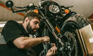 Mechanik z brodą pracuje przy motocyklu. Rozrusznik kręci, a motocykl nie odpala.
