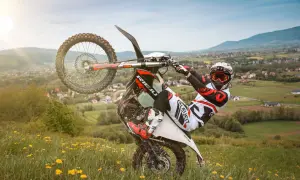 Motocyklista w kasku i goglach wykonuje jazdę na jednym kole na tle malowniczego krajobrazu. Uważaj, bo za takie wyczyny grozi mandat!