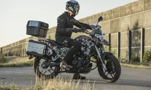 Motocyklista w kasku i czarnej kurtce siedzi na motocyklu Junak RX One 125 z kuframi.