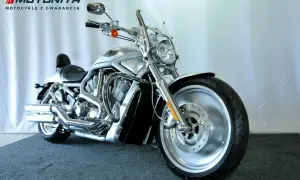 Srebrny motocykl typu cruiser z chromowanymi elementami, na tle białej ściany.