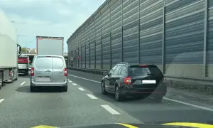 Korek na autostradzie, samochody stoją w rzędzie. Kierowca czarnego kombi zwalnia, by nie dostać mandatu za jazda na suwak.