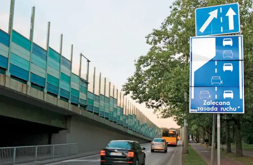 Znak drogowy informuje o zalecanej zasadzie ruchu, czyli jeździe na suwak. Samochody jadą pod ekranami akustycznymi.