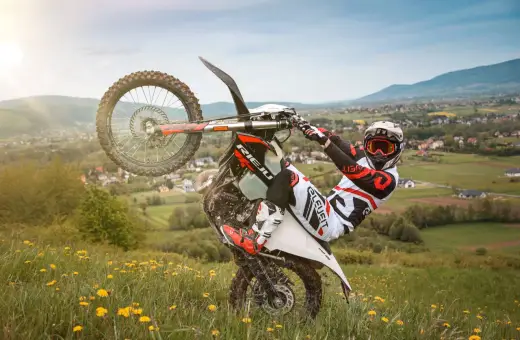 Motocyklista w kasku i goglach wykonuje jazdę na jednym kole na tle malowniczego krajobrazu. Uważaj, bo za takie wyczyny grozi mandat!