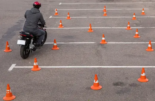 Motocyklista na placu manewrowym, otoczony pomarańczowymi stożkami. Ile jest egzaminów na prawo jazdy? Tyle, ile torów do pokonania!