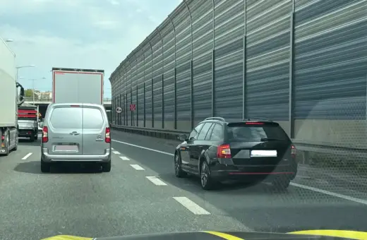 Korek na autostradzie, samochody stoją w rzędzie. Kierowca czarnego kombi zwalnia, by nie dostać mandatu za jazda na suwak.