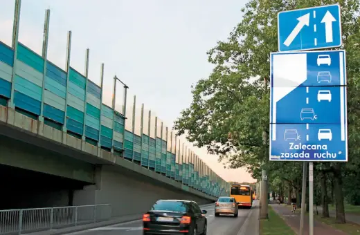 Znak drogowy informuje o zalecanej zasadzie ruchu, czyli jeździe na suwak. Samochody jadą pod ekranami akustycznymi.