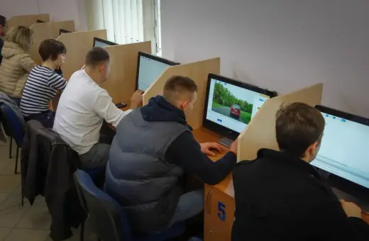 Ludzie siedzą przy komputerach, rozwiązując testy. Zastanawiasz się, ile czasu trwa egzamin teoretyczny na prawo jazdy?