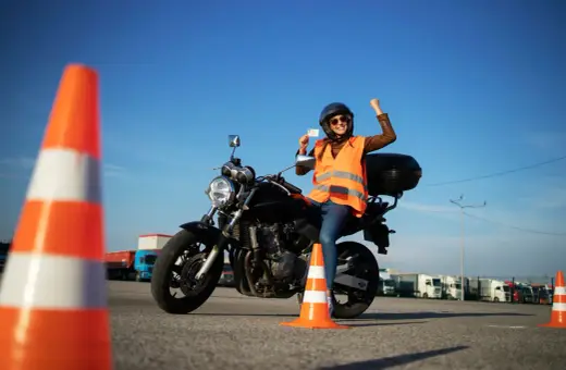 Szczęśliwa motocyklistka z prawem jazdy kategorii A2 na motor 250, świętuje sukces na placu manewrowym.