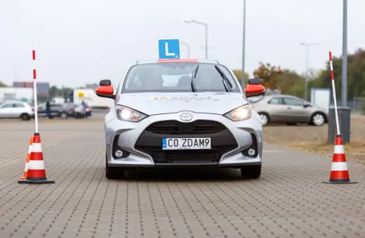 Srebrny samochód nauki jazdy z literą "L" na dachu i pachołkami po bokach. Czas na praktykę po teorii? To auto czeka!