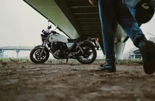 Biały motocykl pod mostem, obok idzie mężczyzna z kaskiem. Zastanawiasz się, jakie prawo jazdy na motor 1000?