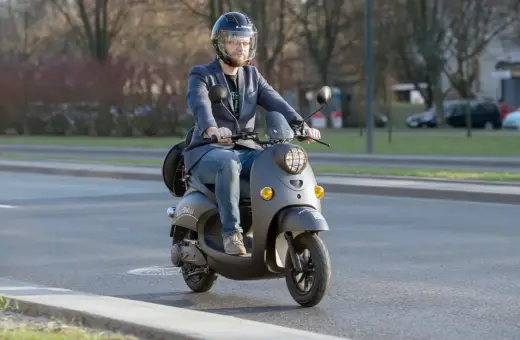 Mężczyzna w kasku jedzie na skuterze. Dowiedz się, od ilu lat można mieć kartę motorowerową, by legalnie poruszać się po drogach.
