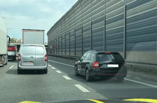Korek na autostradzie, samochody stoją w rzędzie. Kierowca czarnego kombi zwalnia, by nie dostać mandatu za jazda na suwak.