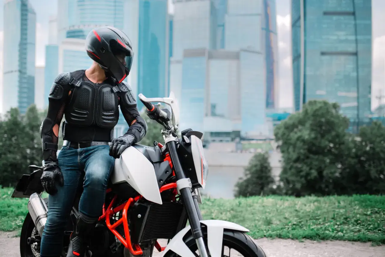 Motocyklista w zbroi ochronnej siedzi na motocyklu na tle wieżowców.