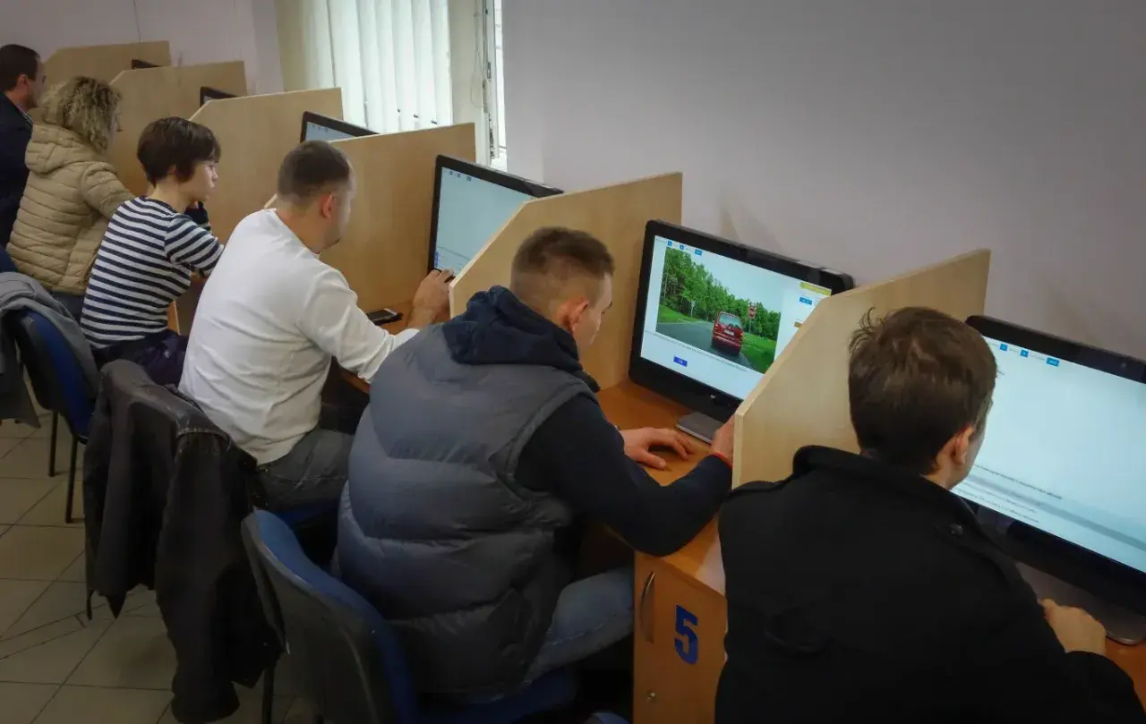 Ludzie siedzą przy komputerach, rozwiązując testy. Zastanawiasz się, ile czasu trwa egzamin teoretyczny na prawo jazdy?