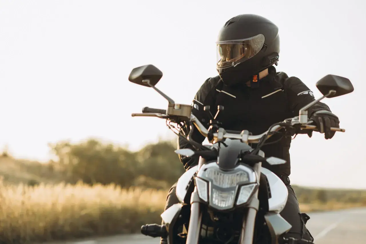 Motocyklista w kasku i kurtce siedzi na motocyklu na tle krajobrazu.
