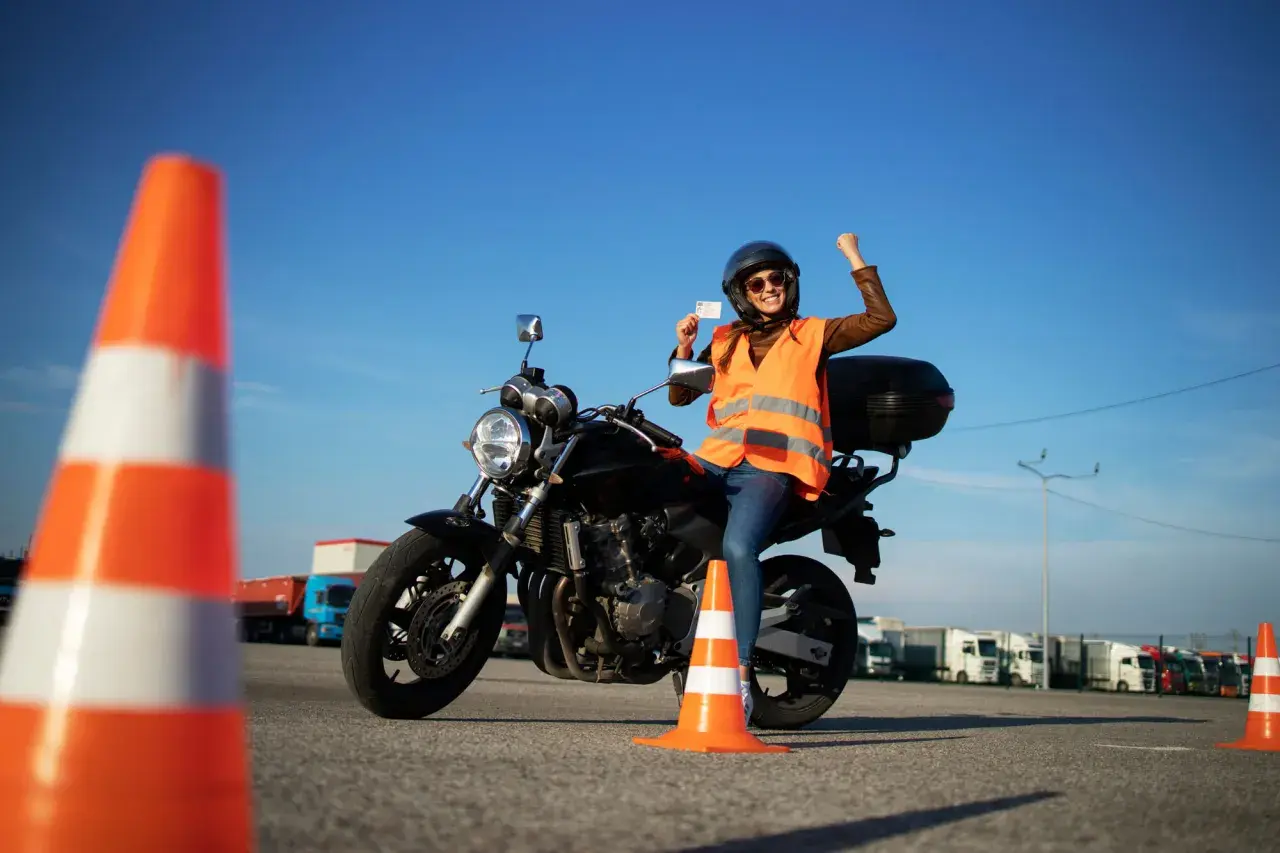 Szczęśliwa motocyklistka z prawem jazdy kategorii A2 na motor 250, świętuje sukces na placu manewrowym.