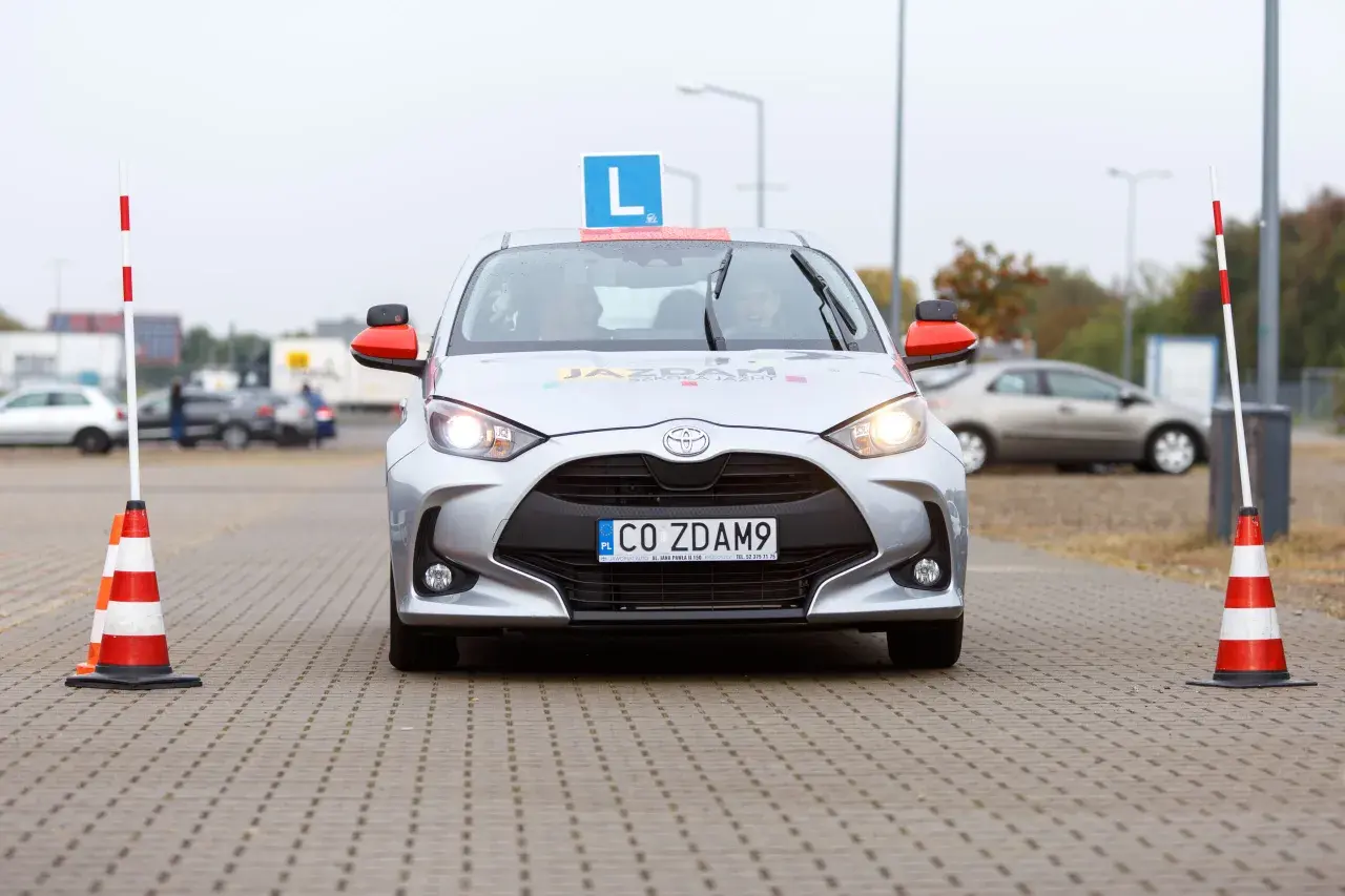 Srebrny samochód nauki jazdy z literą "L" na dachu i pachołkami po bokach. Czas na praktykę po teorii? To auto czeka!