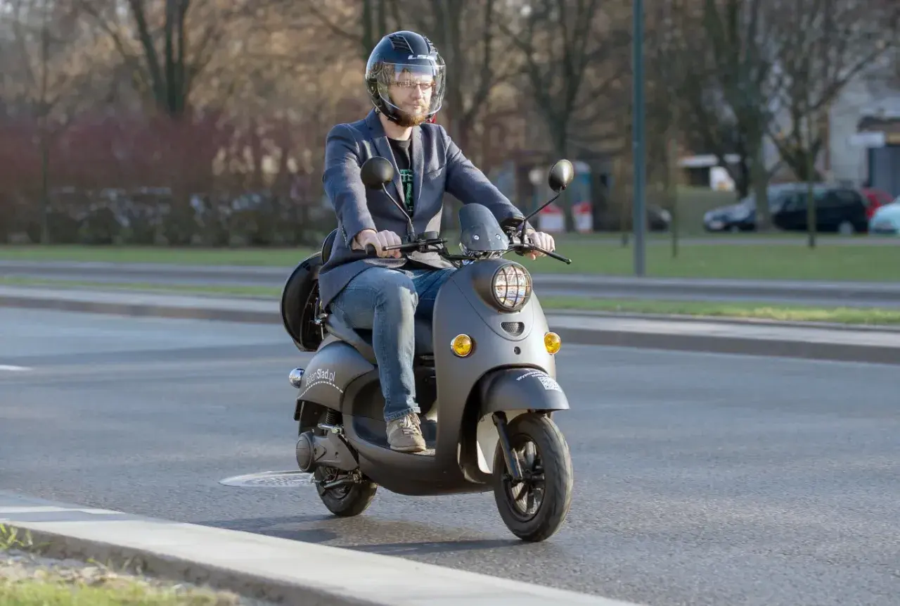 Mężczyzna w kasku jedzie na skuterze. Dowiedz się, od ilu lat można mieć kartę motorowerową, by legalnie poruszać się po drogach.