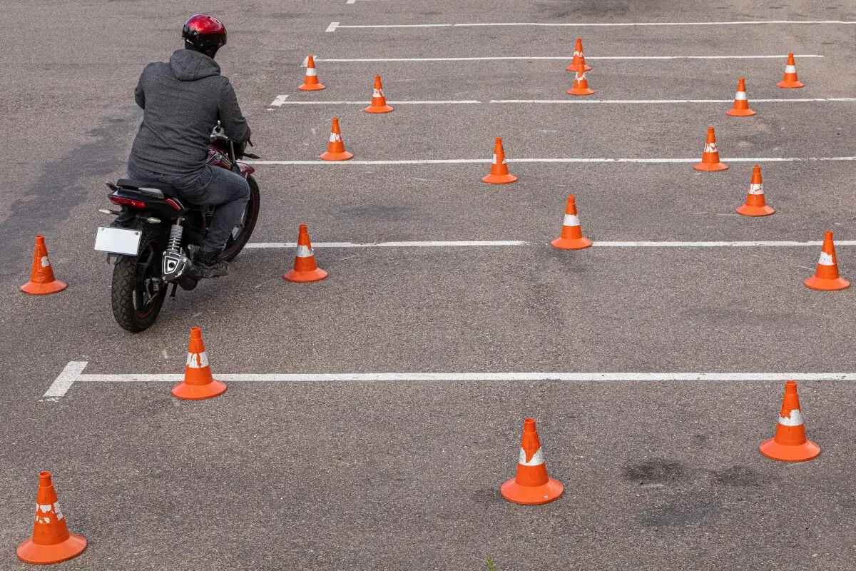 Motocyklista na placu manewrowym, otoczony pomarańczowymi stożkami. Ile jest egzaminów na prawo jazdy? Tyle, ile torów do pokonania!