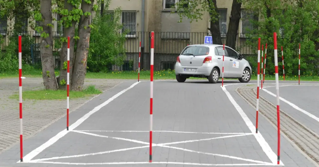 Plac manewrowy z tyczkami i samochodem z literą L. Zastanawiasz się, ile się robi prawo jazdy?