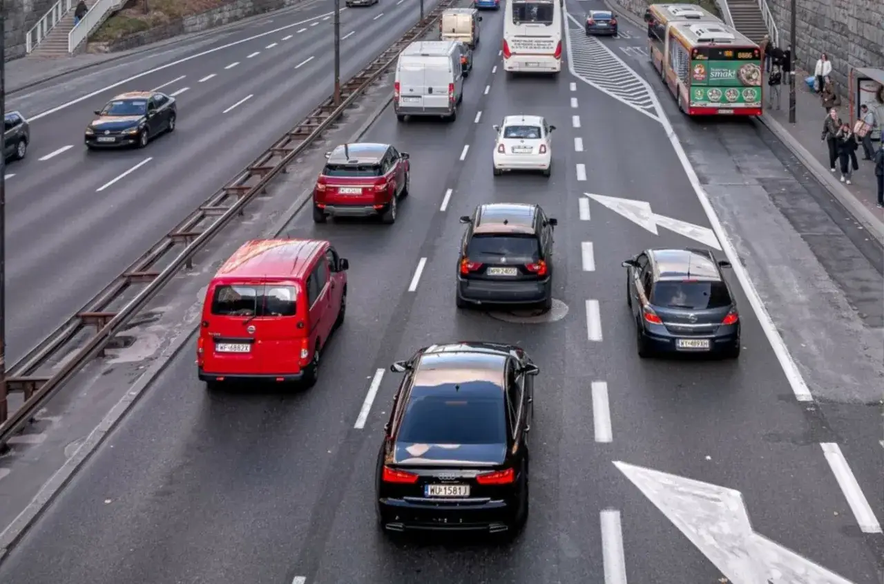Ruch uliczny, gdzie jazda na suwak jest kluczowa, by uniknąć mandatu. Widać różne samochody i autobusy na drodze.