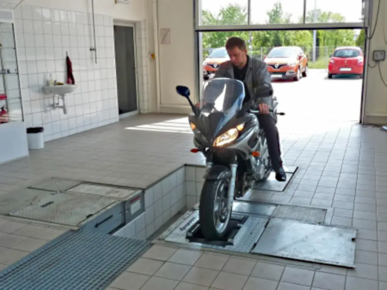 Mężczyzna na motocyklu wjeżdża na stanowisko diagnostyczne. Lepiej zrobić przegląd, niż potem płacić karę za brak przeglądu.