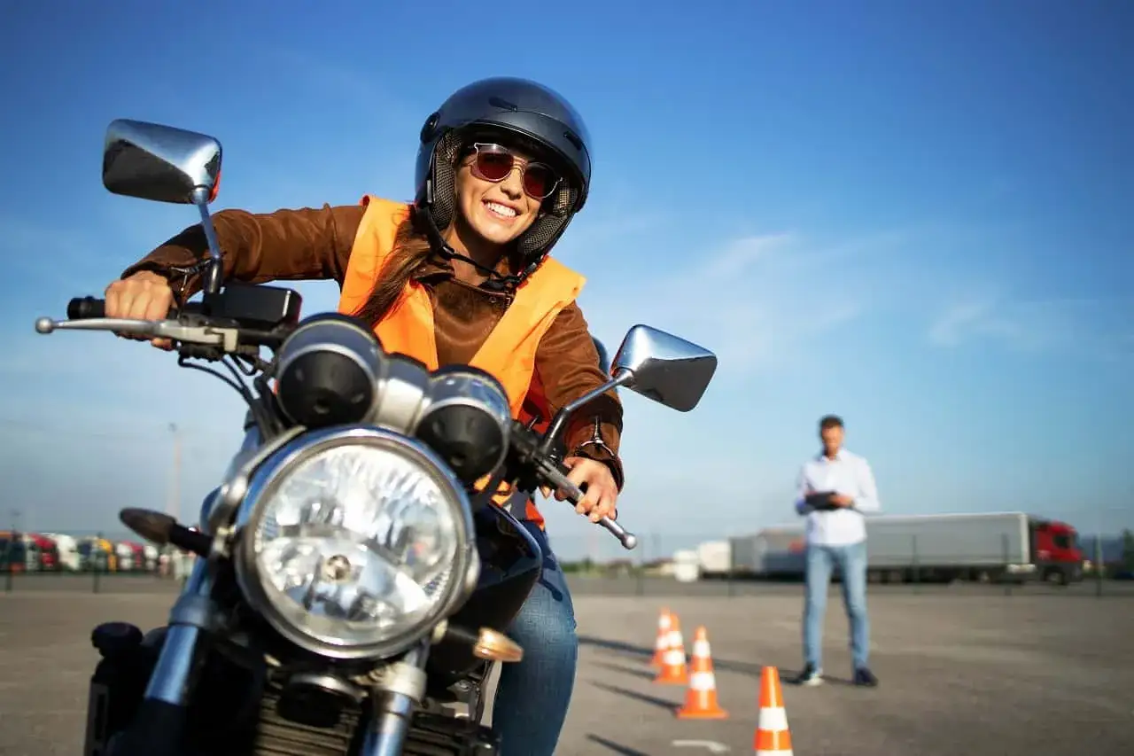Uśmiechnięta kursantka na motorze, w kasku i kamizelce, uczy się manewrów. Zastanawia się, jakie prawo jazdy na motor 1000 będzie potrzebne.